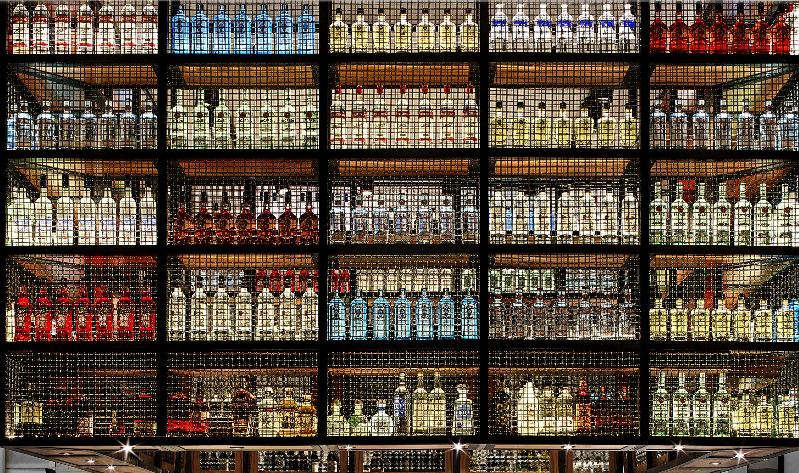 The colored bottles are enhanced by the cabinet lighting, and protected by Banker Wire’s antique brass plated M22-37.