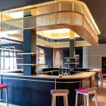 A contemporary wine tasting space features M22-83 brass woven wire mesh as a ceiling gantry that forms a sculptural canopy above the bar.